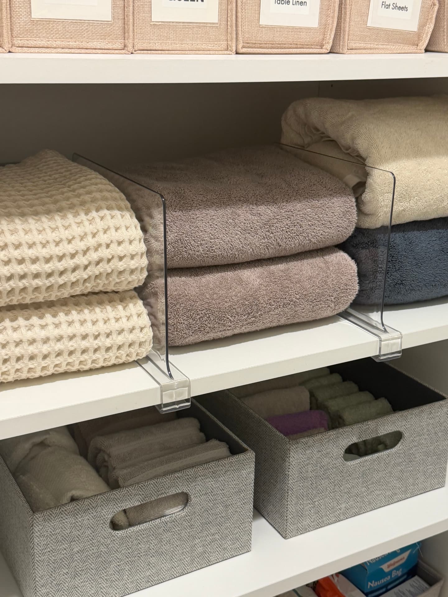 Bath towels separated by clear shelf dividers above baskets of rolled washcloths