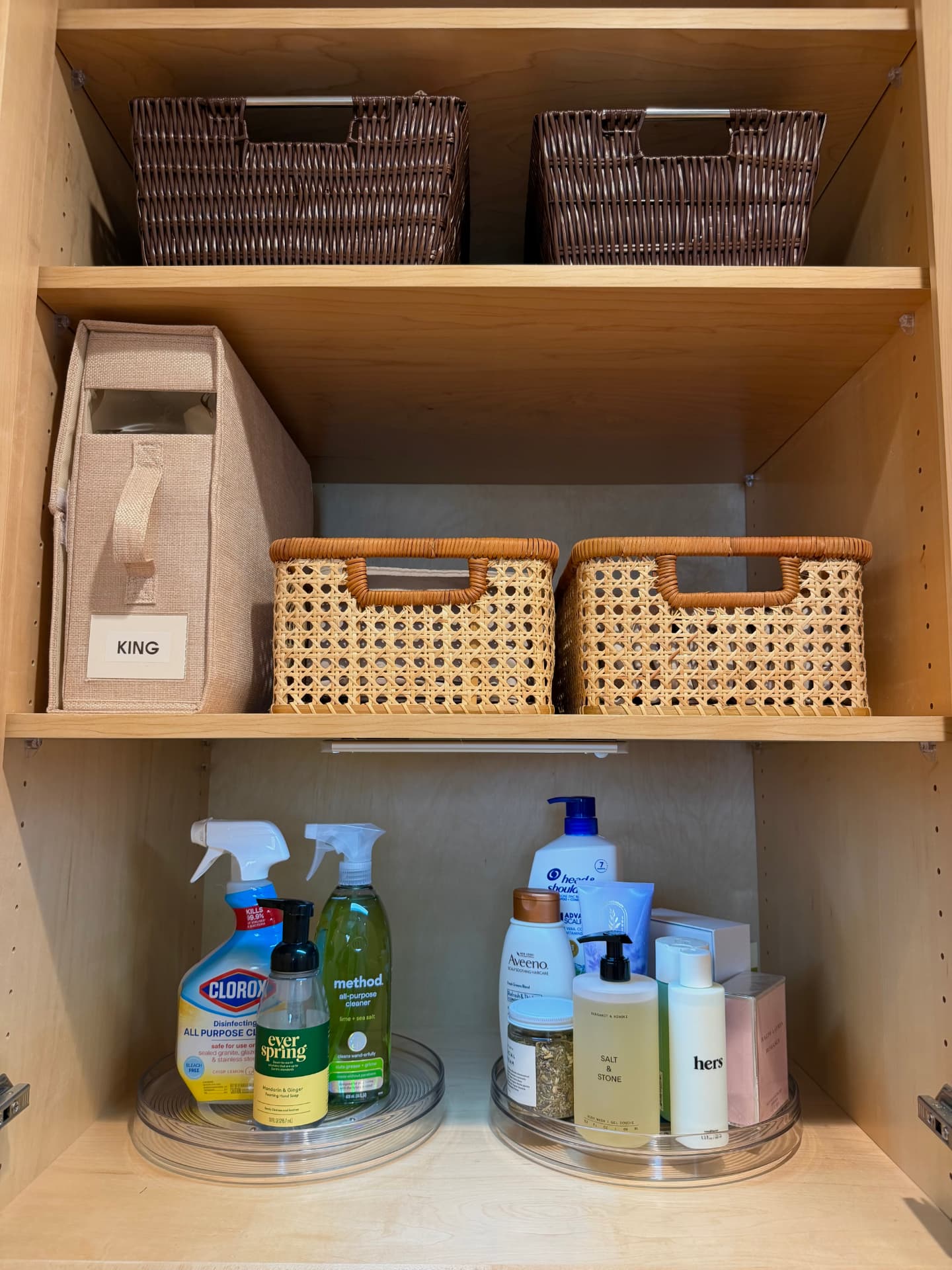 Upper shelves with dark woven baskets, a labeled king bin beside cane baskets, and two clear turntables of cleaning and skincare bottles