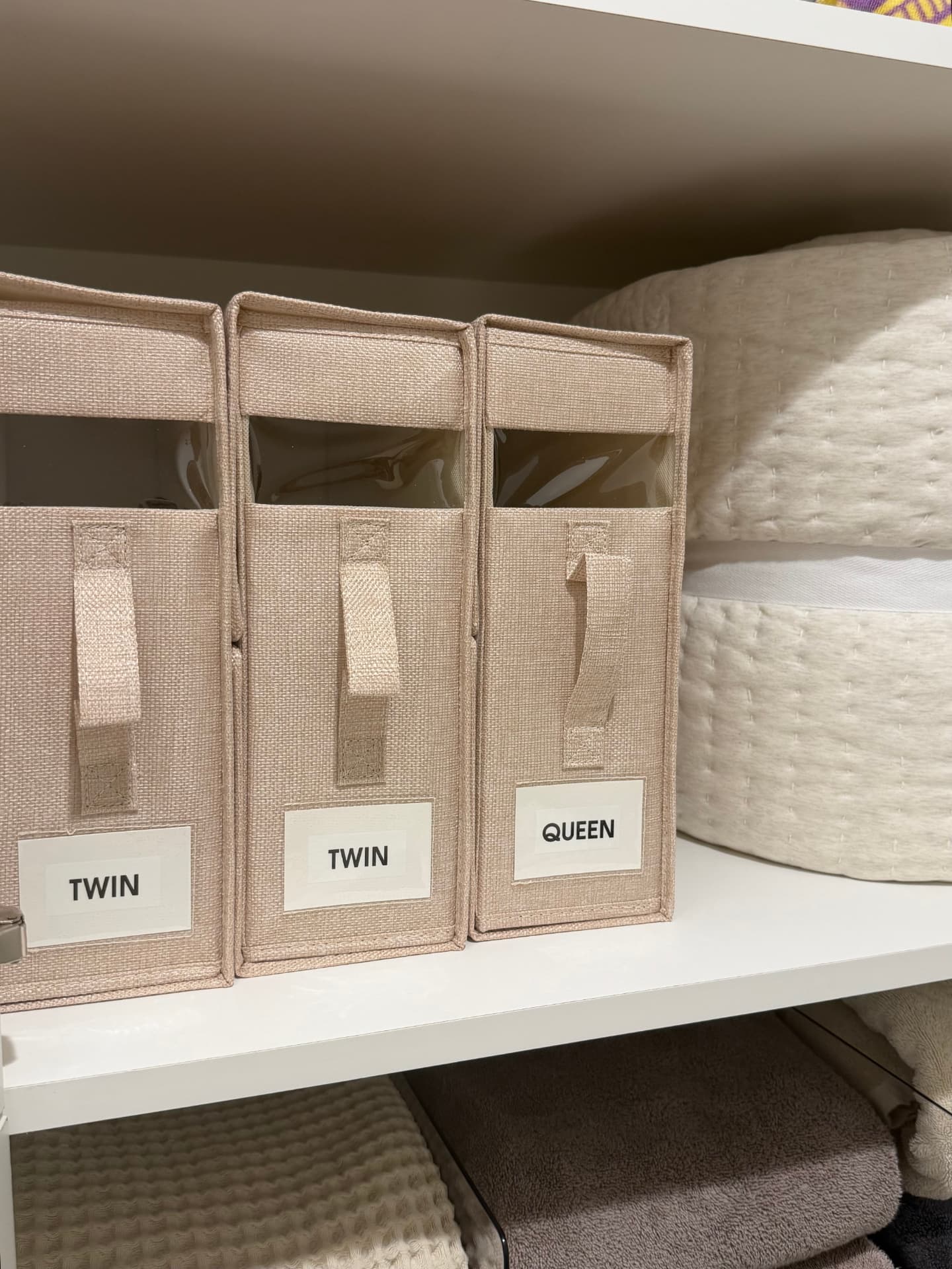 Labeled twin and queen sheet bins beside rolled quilted comforters