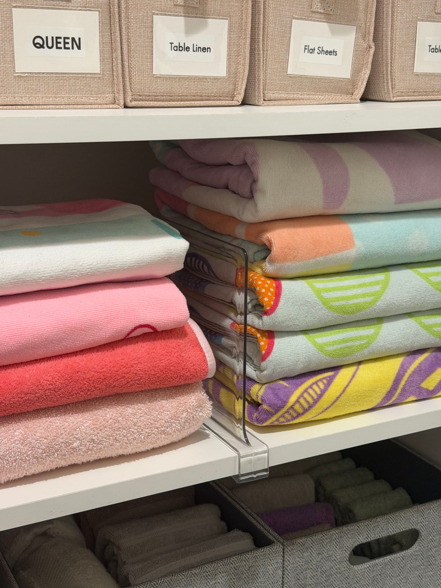 Beach towels folded in stacks with a clear shelf divider below labeled linen bins