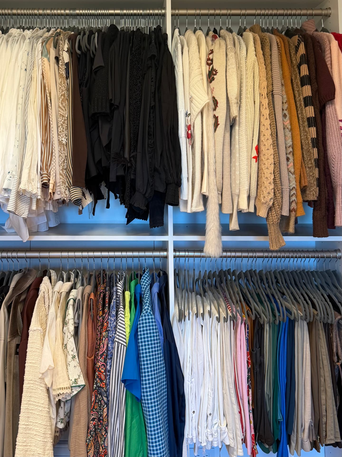 Two rails of color-sorted tops, blouses, and knit sweaters across white closet shelves