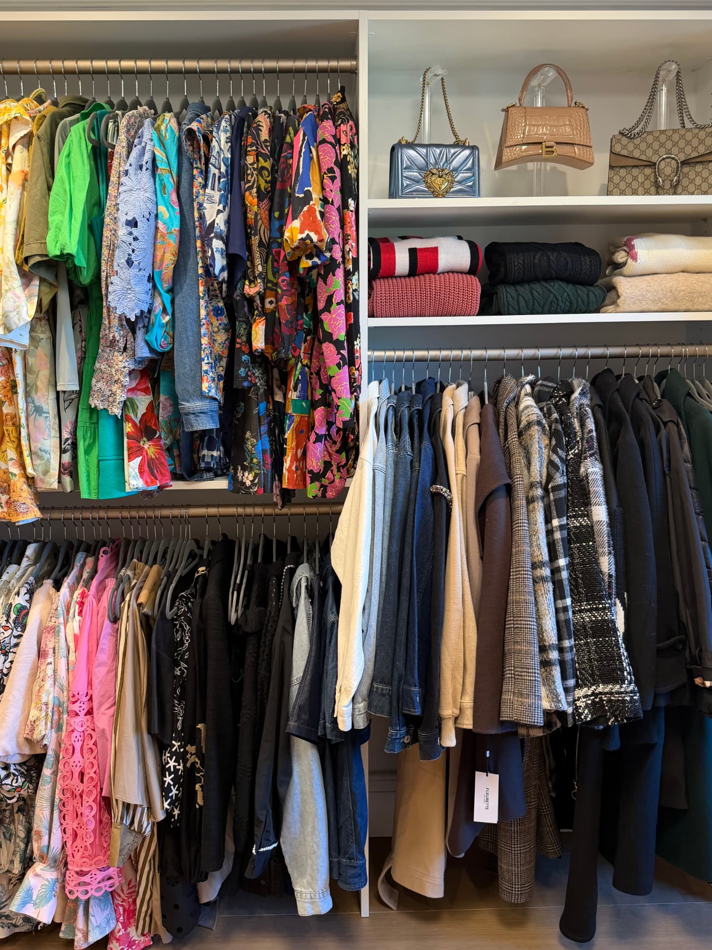 Hanging section with colorful floral dresses and bright tops on the left, dark coats and jackets on the right, and handbags displayed on the white shelf above