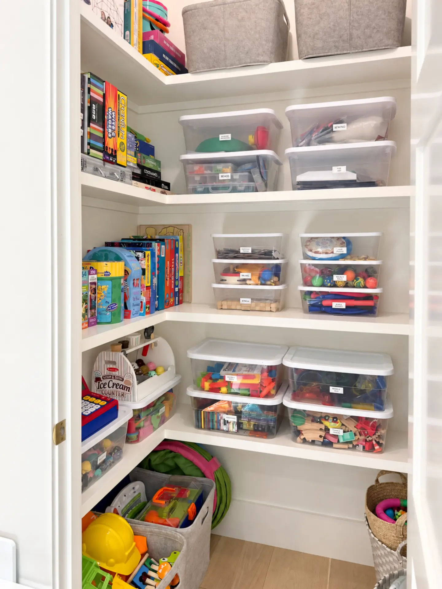 Playroom closet corner with board games, a toy caddy, and stacked labeled bins of craft and building toys