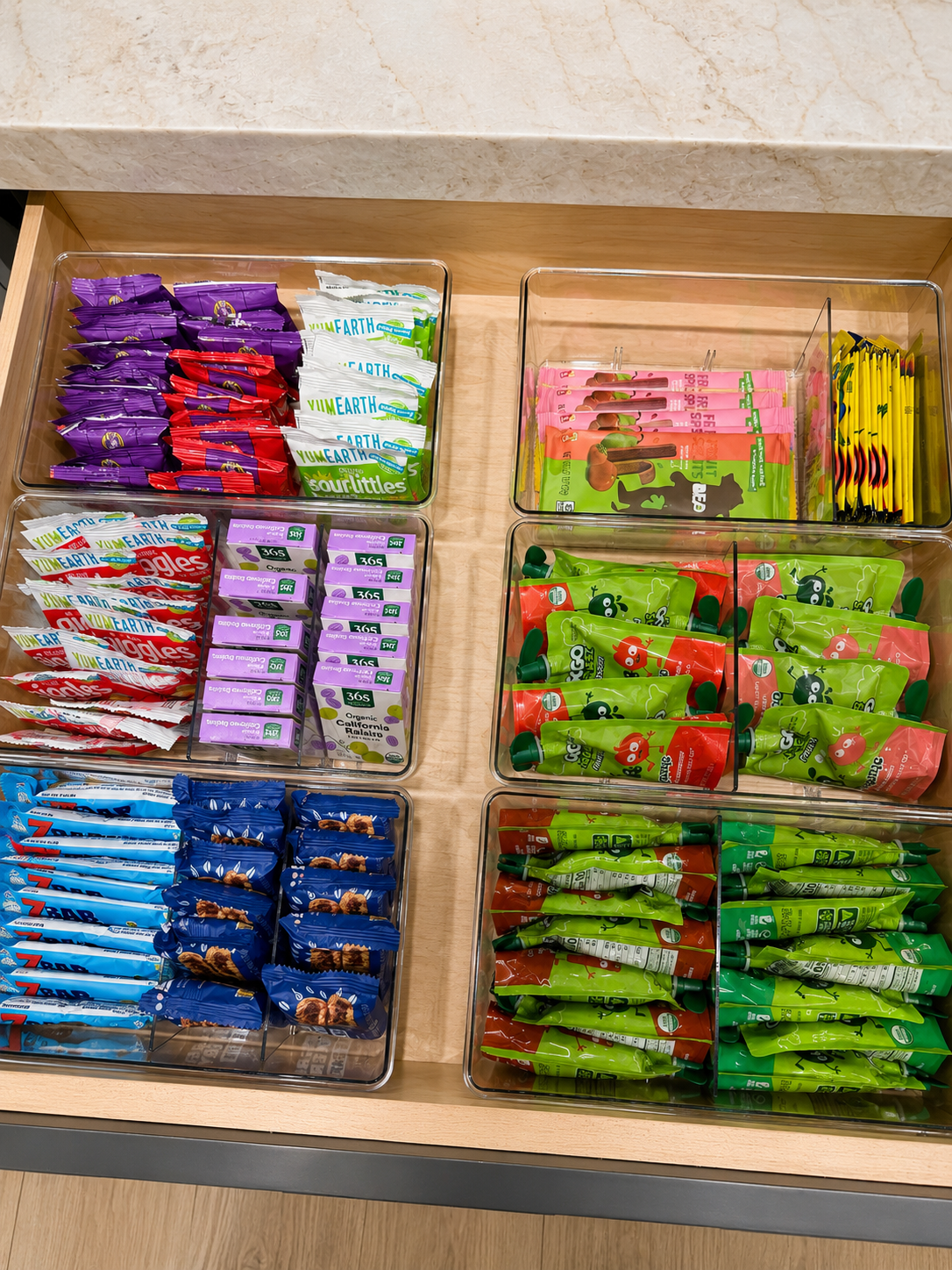 Drawer of clear divided bins holding children's snacks sorted by type, including fruit straps, gummies, and squeeze pouches